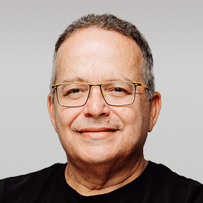 A middle-aged man with short, gray hair and glasses, wearing a black shirt, smiling slightly against a plain light background.